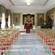 A regal reception room with chairs, a piano and a podium with a sign that reads Hillsborough Castle